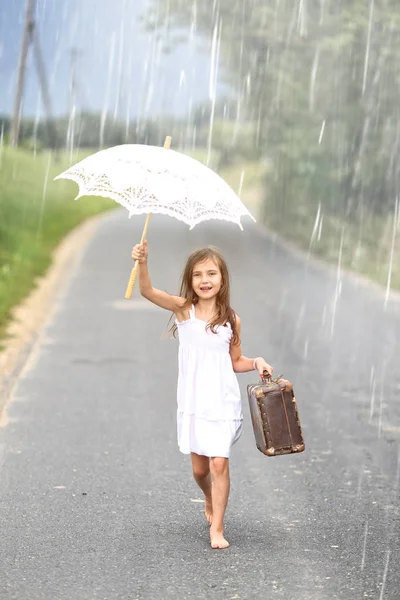 Chica joven camina con maleta y paraguas en la lluvia —  Fotos de Stock