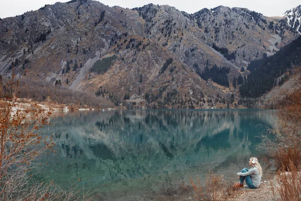 Mulher ouvindo música na beira da água do lago da montanha — Fotografia de Stock