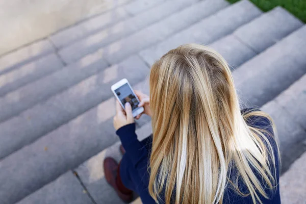 Affärskvinna sitter på stadens trappsteg och håller smartphon — Stockfoto