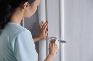 Kadın kapı kolunu dezenfekte beziyle temizliyor.