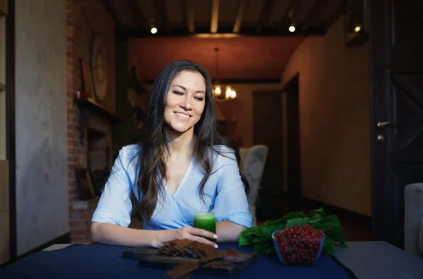Smiling vegetarian woman sitting at the table with celery fresh juice, flaxseed bread and berries