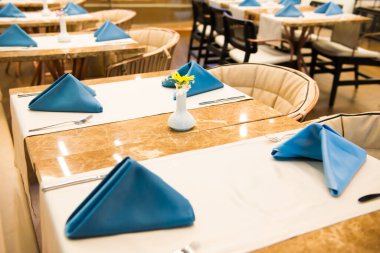 Lokantada masa örtüleri ve peçetelerle süslenmiş boş yemek masaları.