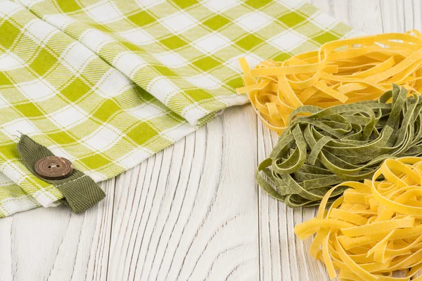 Pastas verdes y amarillas crudas sobre una vieja mesa de madera blanca . — Foto de Stock