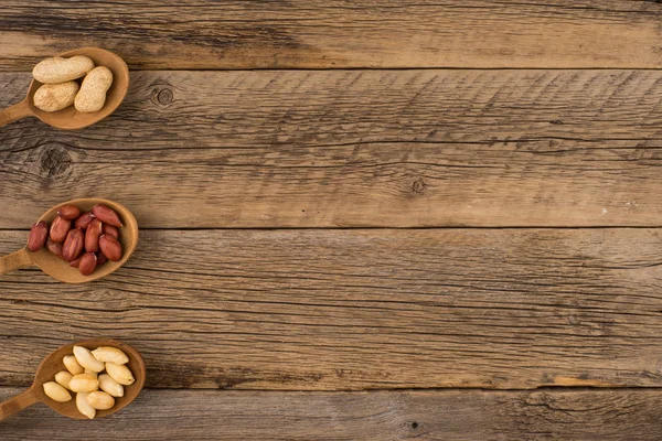 Cacahuetes en cucharas de madera sobre un fondo de madera viejo . — Foto de Stock