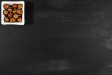 Kara tahta üzerinde beyaz bir kase fındık. 