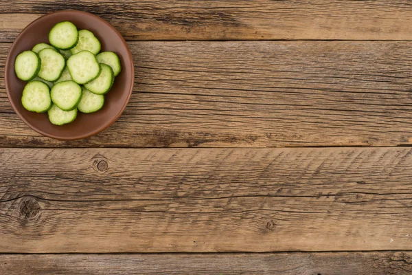 Sliced cucumbers in a brown plate on old wooden table. — Stock Photo, Image