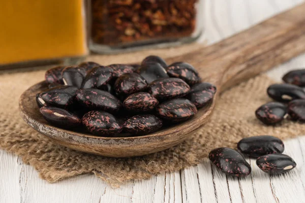 Black beans in a wooden spoon on old wooden table. — Stock Photo, Image