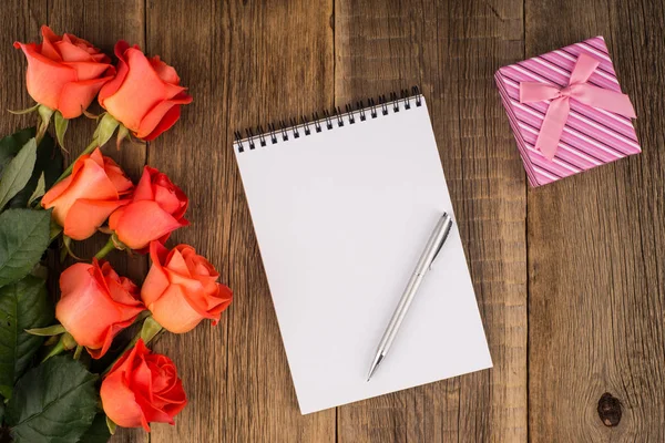 Blank notebook, pen with a rose and a gift on a wooden table. — Stock Photo, Image