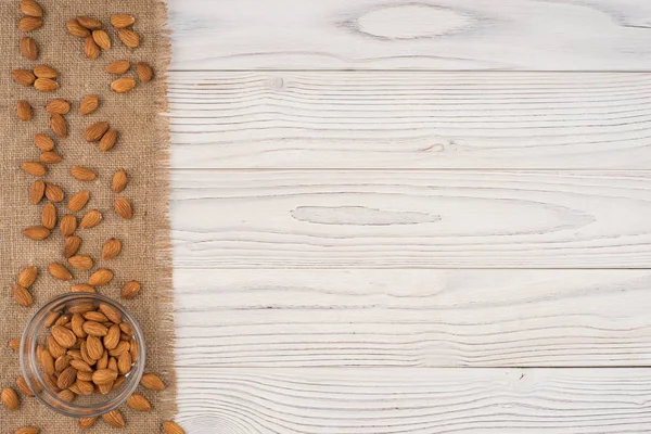 Almendras en un tazón de vidrio y una vieja mesa de madera blanca . —  Fotos de Stock