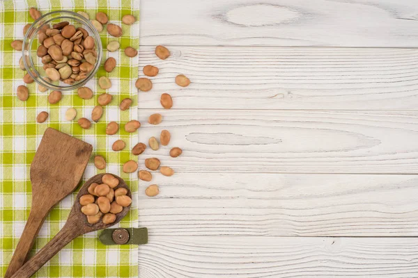 Frijoles en un tazón de vidrio y una cuchara de madera sobre una mesa blanca . —  Fotos de Stock