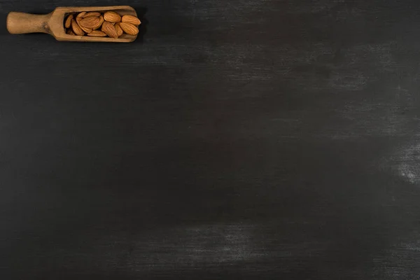 Mandeln in einer hölzernen Schaufel in einer schwarzen Tafel. — Stockfoto