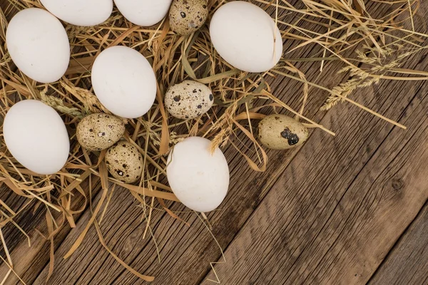 Chicken and quail eggs in a straw and a wooden table. — Stock Photo, Image