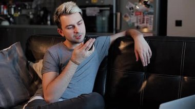 Genç bir adam evdeki akıllı telefonuna bir sesli mesaj kaydediyor.