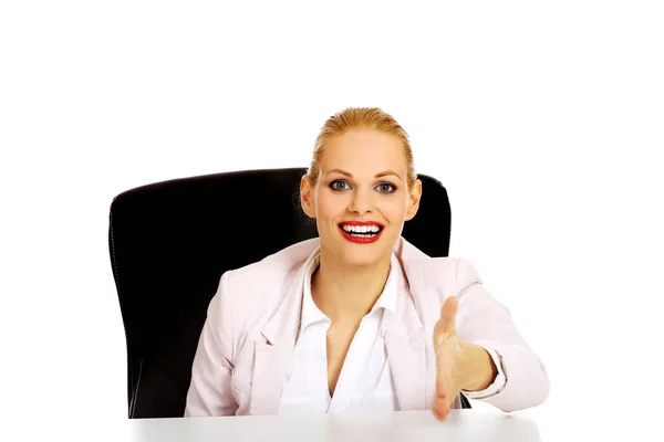 握手のための開いた手の準備ができたと机の後ろに座っているビジネス女性を笑顔します。 — ストック写真