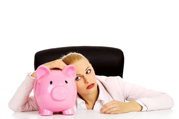 Besorgte Geschäftsfrau mit Sparschwein hinter dem Schreibtisch — Stockfoto