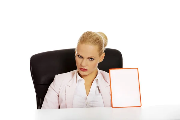 Serious business woman sitting behind the desk and holding board with ban — Stock Photo, Image