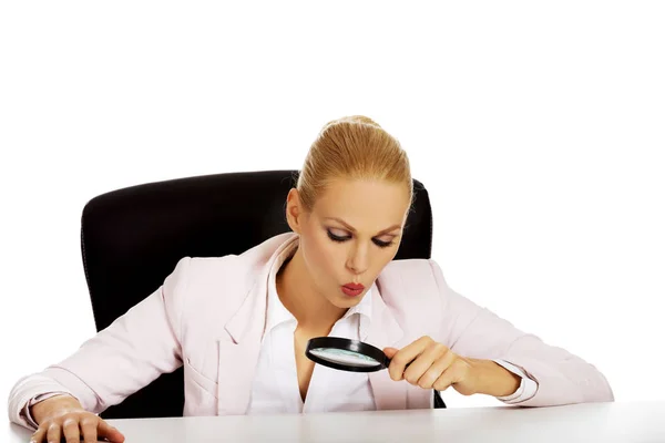 Mulher de negócios sentada atrás da mesa e olhando para uma lupa — Fotografia de Stock