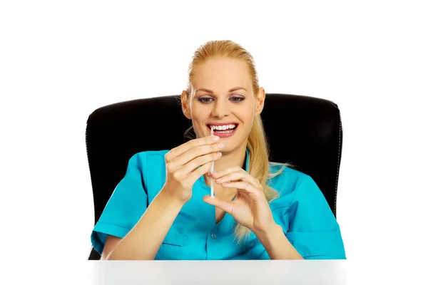 Забавна жінка-лікар або медсестра сидить за столом і тримає шприц — стокове фото