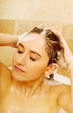 Genç, rahatlatıcı kadın banyoda saç yıkıyor.