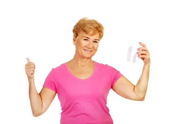 Smiling senior woman holding a tooth model and shows OK — Stock Photo, Image