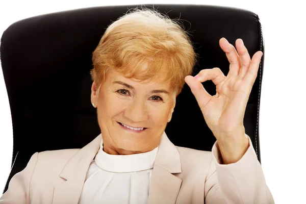 Sorridi anziana donna d'affari seduta sulla poltrona e mostra il segno ok — Foto Stock