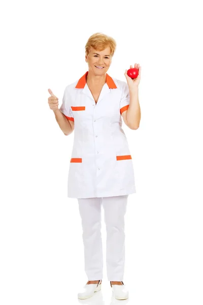 Sourire femme âgée médecin ou infirmière tenant jouet rouge coeur — Photo