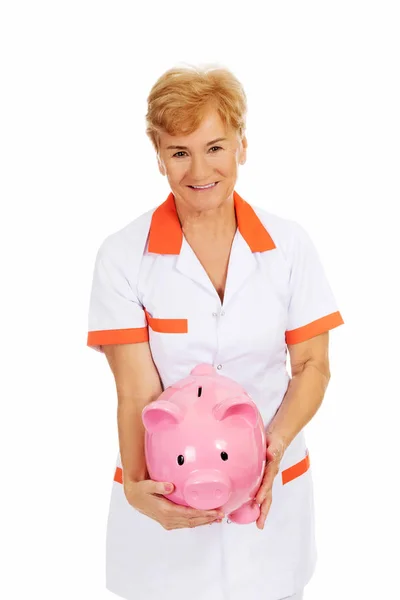 Idős női orvos vagy a nővér gazdaság piggybank mosoly — Stock Fotó