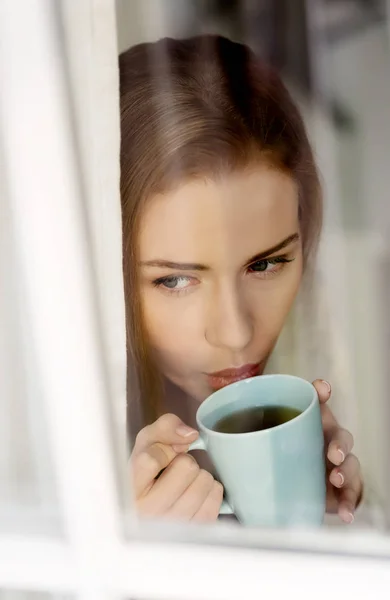 Belle femme caucasienne buvant du café chaud ou du thé et regardant par la fenêtre . — Photo