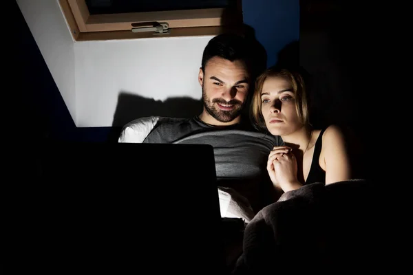 Jeune couple avec ordinateur portable regarder un film au lit — Photo