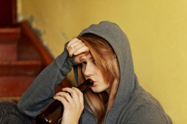 Genç bunalımlı kadın merdivenlerde oturuyor ve bira içiyor.