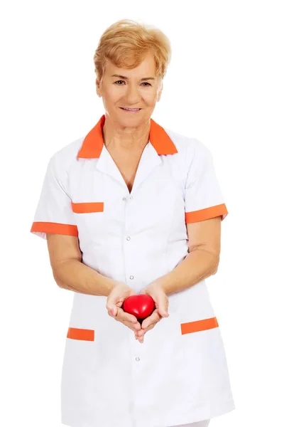 Sorria médico idoso ou enfermeira segurando coração de brinquedo vermelho — Fotografia de Stock