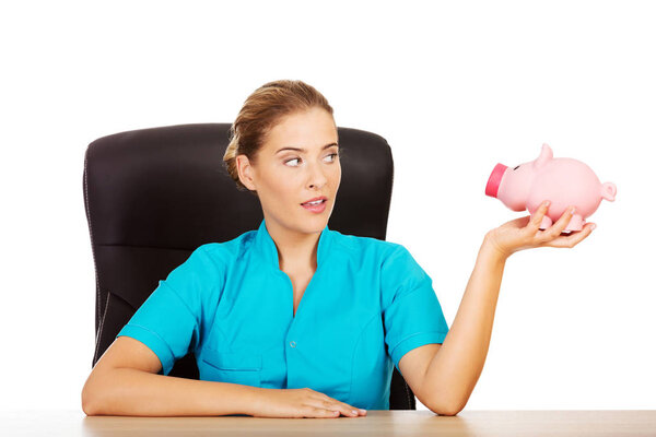 Young female doctor or nurse holding piggybank
