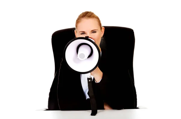 Business woman sitting behind the desk and screaming through a megaphone — Stock Photo, Image