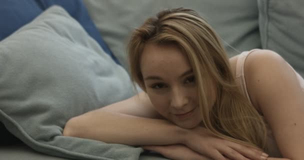 Frau liegt lächelnd auf Couch und blickt in Kamera — Stockvideo