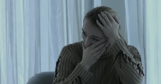 Triste mulher deprimida em casa sentada no sofá, olhando para baixo e tocando sua testa . — Vídeo de Stock