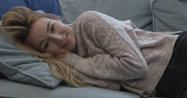 Mulher deitada no sofá sorrindo e olhando para a câmera — Vídeo de Stock