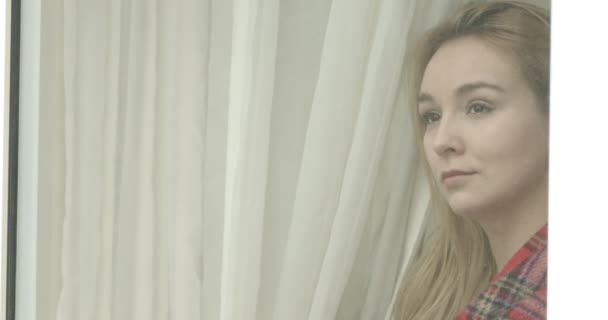 Beautiful young woman looking through window. — Stock Video