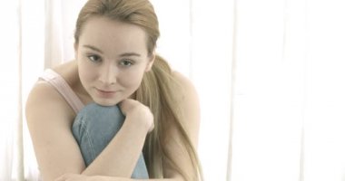 Güzel, gülümseyen bir kadın oturma odasında kameraya bakıyor.