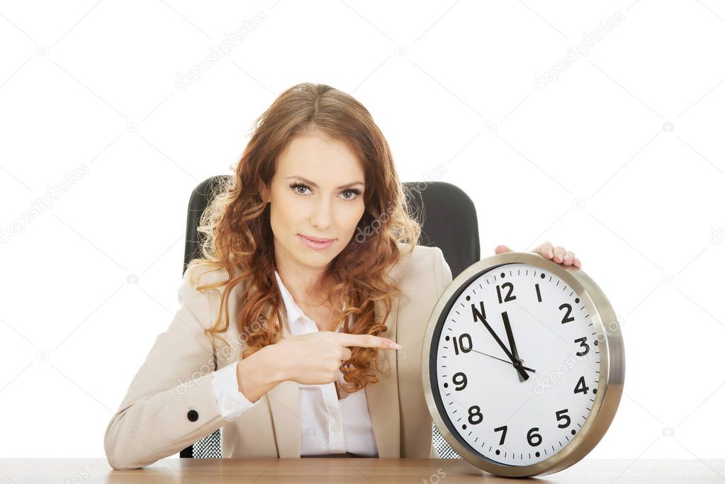 Businesswoman pointing on a clock by a desk.