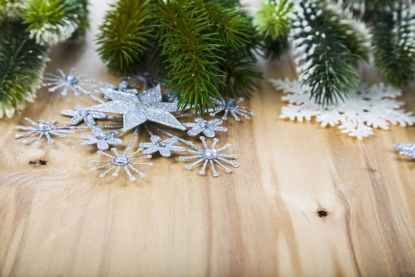 Ασημί νιφάδες χιονιού και κλαδιά έλατου σε ένα ξύλινο τραπέζι. Χριστούγεννα — Φωτογραφία Αρχείου
