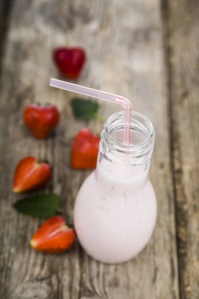 Smoothies e morango maduro em uma mesa de madeira. Bebida láctea com — Fotografia de Stock