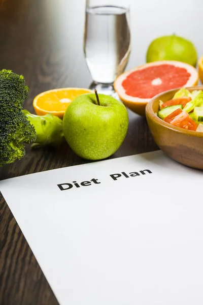 Comida e folha de papel com um plano de dieta em uma mesa de madeira escura . — Fotografia de Stock