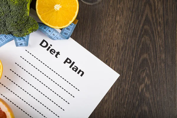 Voedsel en vel papier met een dieetplan op een donkere houten tafel. — Stockfoto