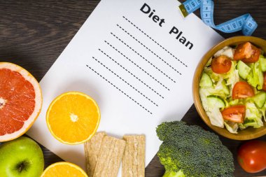 Gıda ve koyu ahşap bir masa üzerinde bir diyet planı ile kağıt.