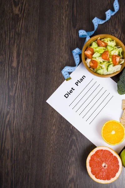 Gıda ve koyu ahşap bir masa üzerinde bir diyet planı ile kağıt.