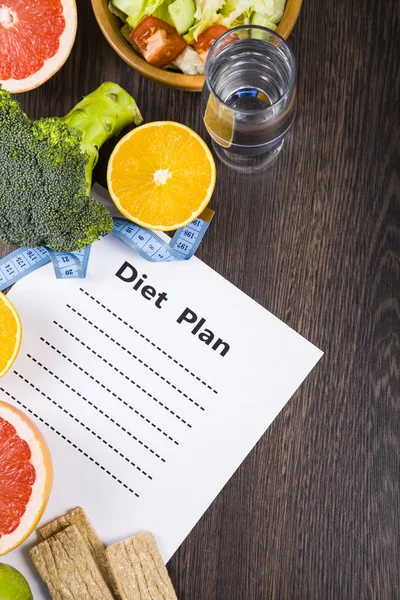 Voedsel en vel papier met een dieetplan op een donkere houten tafel. — Stockfoto