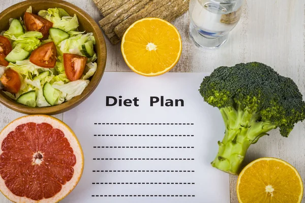 Comida e folha de papel com um plano de dieta em uma mesa de madeira . — Fotografia de Stock