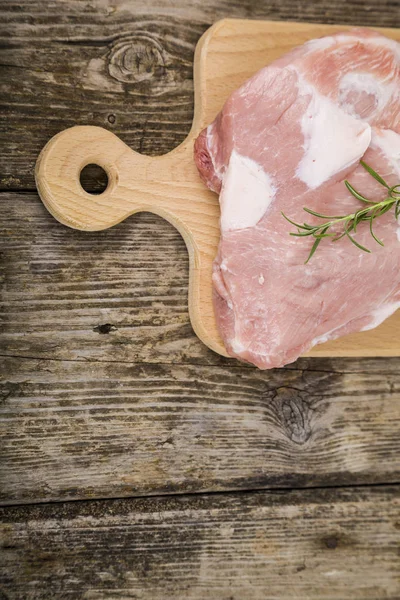 テーブルの上の木の板にローズマリーと生の豚肉. — ストック写真