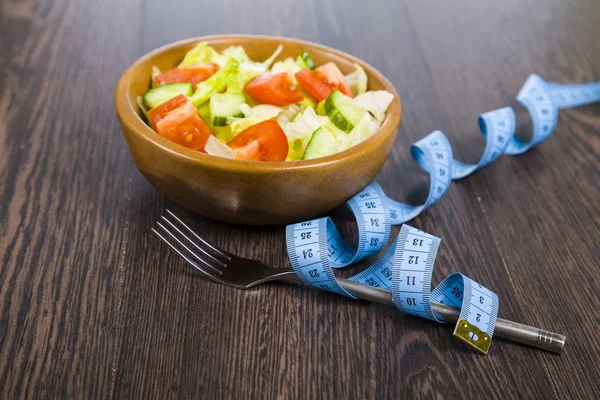 Salad in wooden bow, fork and measuring tape on a dark table clo — Stock Photo, Image