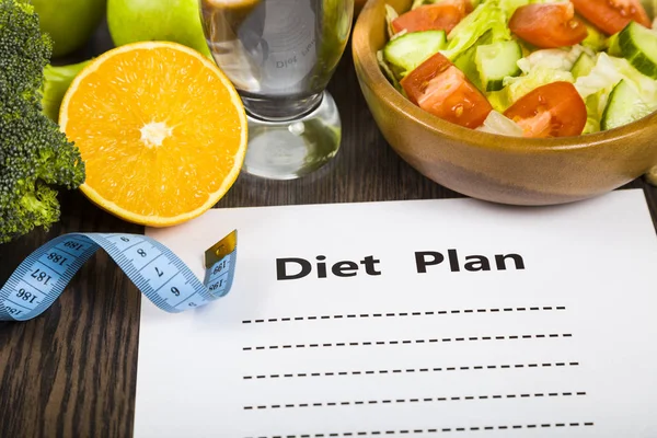 Gıda ve koyu ahşap bir masa üzerinde bir diyet planı ile kağıt.